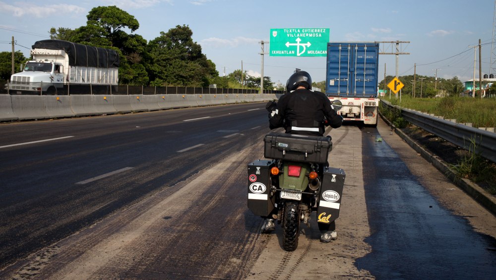 Nathaniel does a systems check on his bike (and himself) after a car accessories vendor helped him to an oil free stretch of pavement. Photo: Alex Washburn