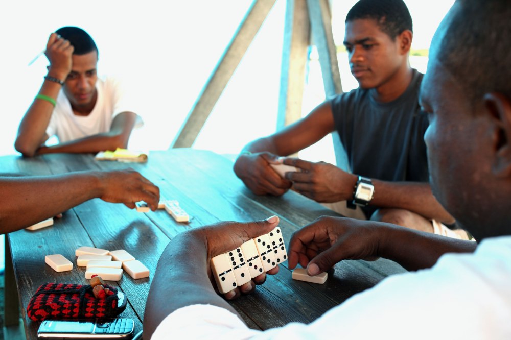 A group of locals concentrates on their game of dominos in the shade next to the only gas station in Placencia Belize. Photo: Alex Washburn