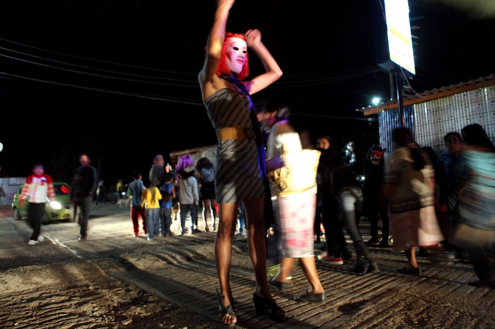 A man dressed in drag dances and poses in the lights of a police vehicle as the residents of Tule Mexico exit the city cemetery following a dance party on November 2, 2013.